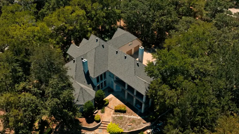 Angled aerial view of a completed grey shingle roof on a two storey home with two chimneys and a detached garage
